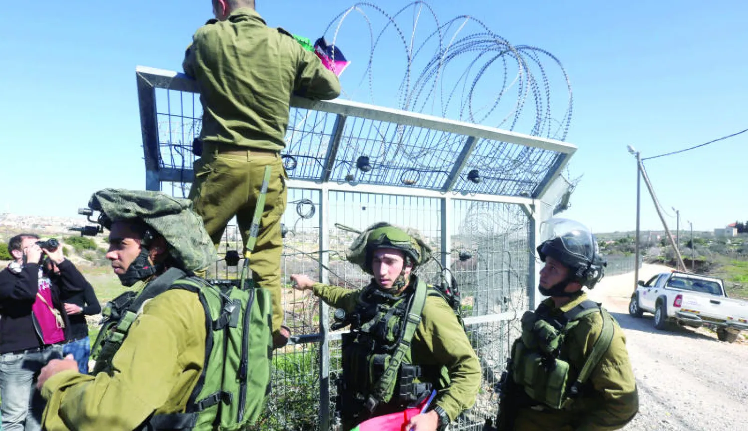 جنود إسرائيليون يزيلون أعلاما فلسطينية بعد مظاهرة نظمها فلسطينيون أمس في بلدة بيت عمر احتجاجا على القرار الإسرائيلي ببناء 450 وحدة استيطانية جديدة (إ.ب.أ)