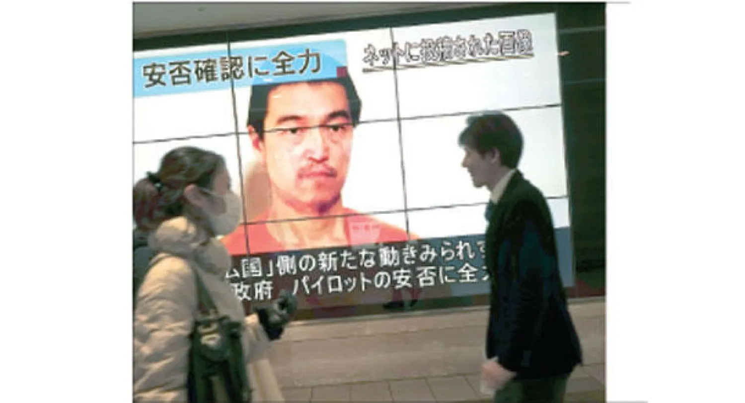 مواطنان يابانيان يمران في العاصمة طوكيو بجوار شاشة تلفزيون عملاقة ظهر عليها الرهينة كينجي غوتو الذي أعلنت «داعش» إعدامه أمس (أ.ب)