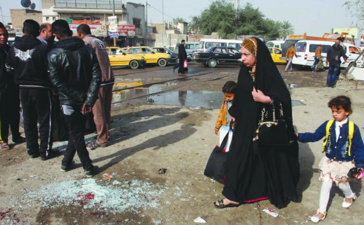 إمرأة مع طفليها يمرون بالقرب من مكان تفجير انتحاري في ساحة عدن بمنطقة الكاظمية في بغداد  أمس (رويترز)