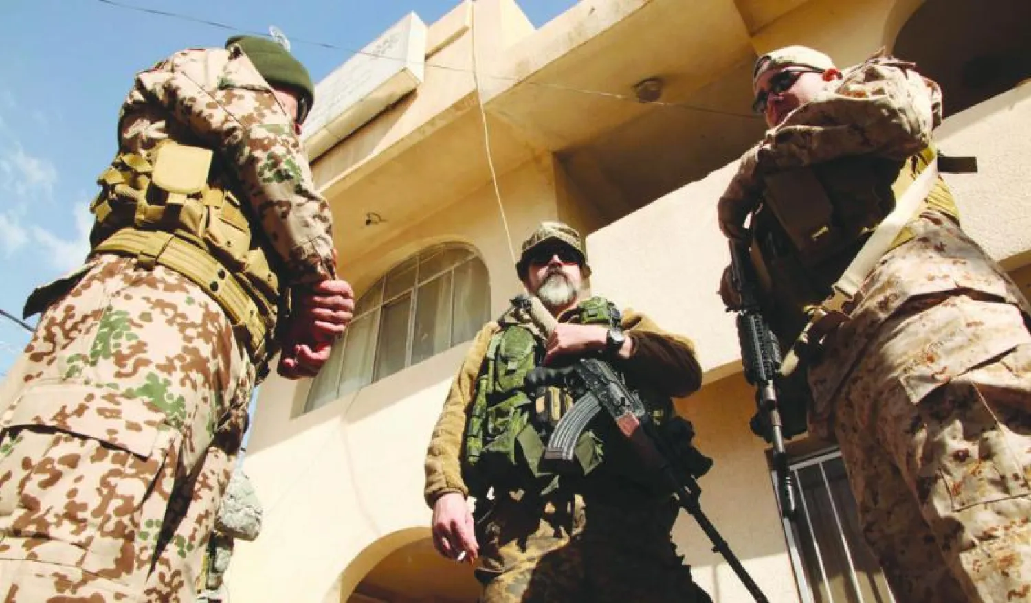 الأميركي سكوت الذي انضم إلى الفصيل المسيحي المسلح «دويخ نوشا» يحمل سلاحه متوسطا مسلحين آخرين أمام مقر حزب آشوري في دهوك بإقليم كردستان العراق (رويترز)