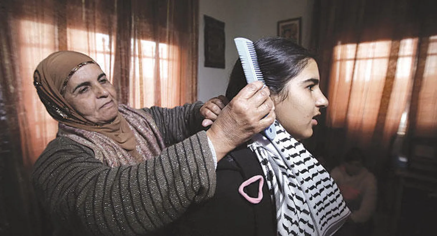 والدة ملاك الخطيب تمشط لها شعرها في بيت العائلة بالضفة الغربية (أ.ف.ب)