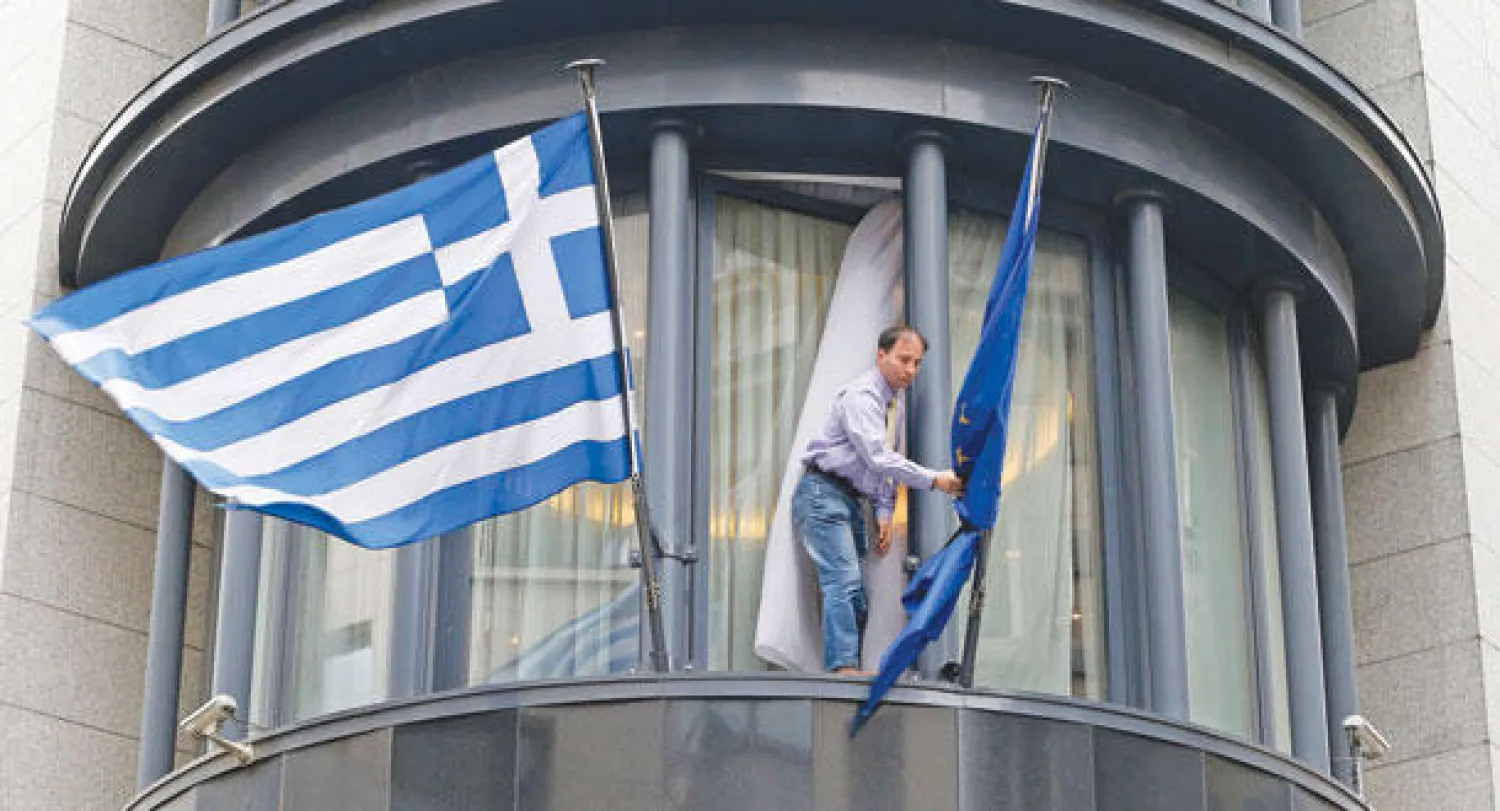 رجل يقوم برفع العلم الأوروبي بجانب اليوناني على مبنى السفارة اليونانية في بروكسل أمس (رويترز)