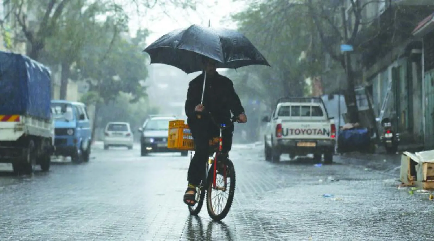 فلسطيني يحتمي بمظلة من الأمطار الغزيرة التي ضربت جل المدن الفلسطينية أمس (أ.ف.ب)