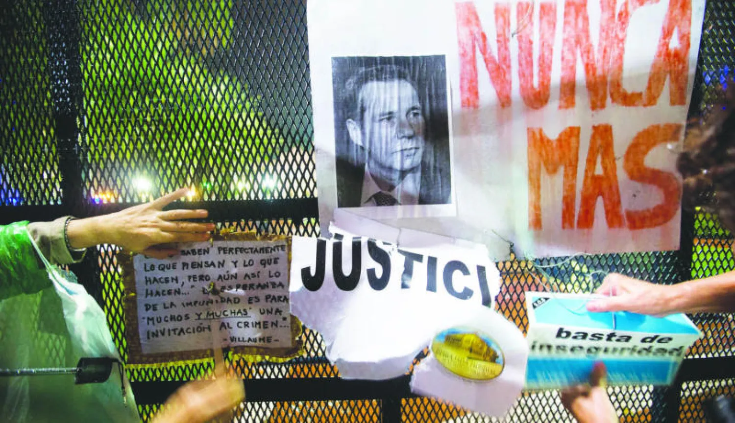 متظاهرون أرجنتينيون يعلقون ملصقات على حاجز في نهاية مسيرة نظمها في بوينس أيرس اتحاد المدعين العامين للمطالبة بكشف ملابسات وفاة زميل لهم في المهنة بعد مرور شهر على وفاته (أ.ب)