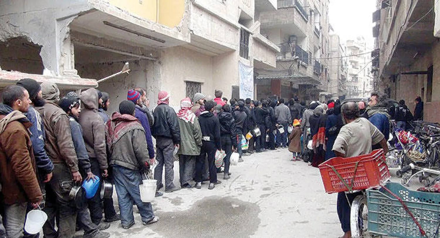 سوريون وفلسطينيون بمخيم اليرموك المحاصر من قبل النظام يصطفون في طوابير لتسلم الطعام من جمعية خيرية (أ.ف.ب)