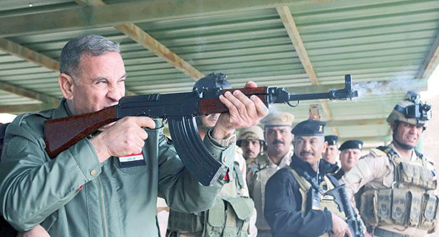 وزير الدفاع العراقي خالد العبيدي يطلق النار من بندقية خلال زيارته لمعسكر التاجي شمال بغداد أمس (رويترز)