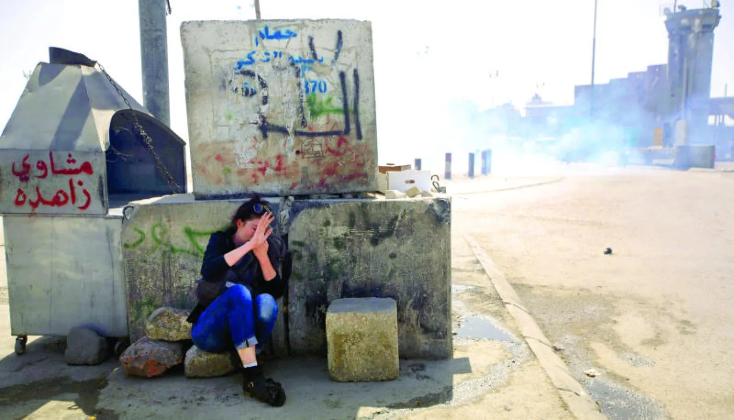 فلسطينية تحتمي من الغاز المسيل للدموع الذي أطلقه جنود إسرائيليون خلال مسيرة عشية اليوم العالمي للمرأة عند معبر قلندية بين القدس المحتلة ورام الله أمس (أ.ب)