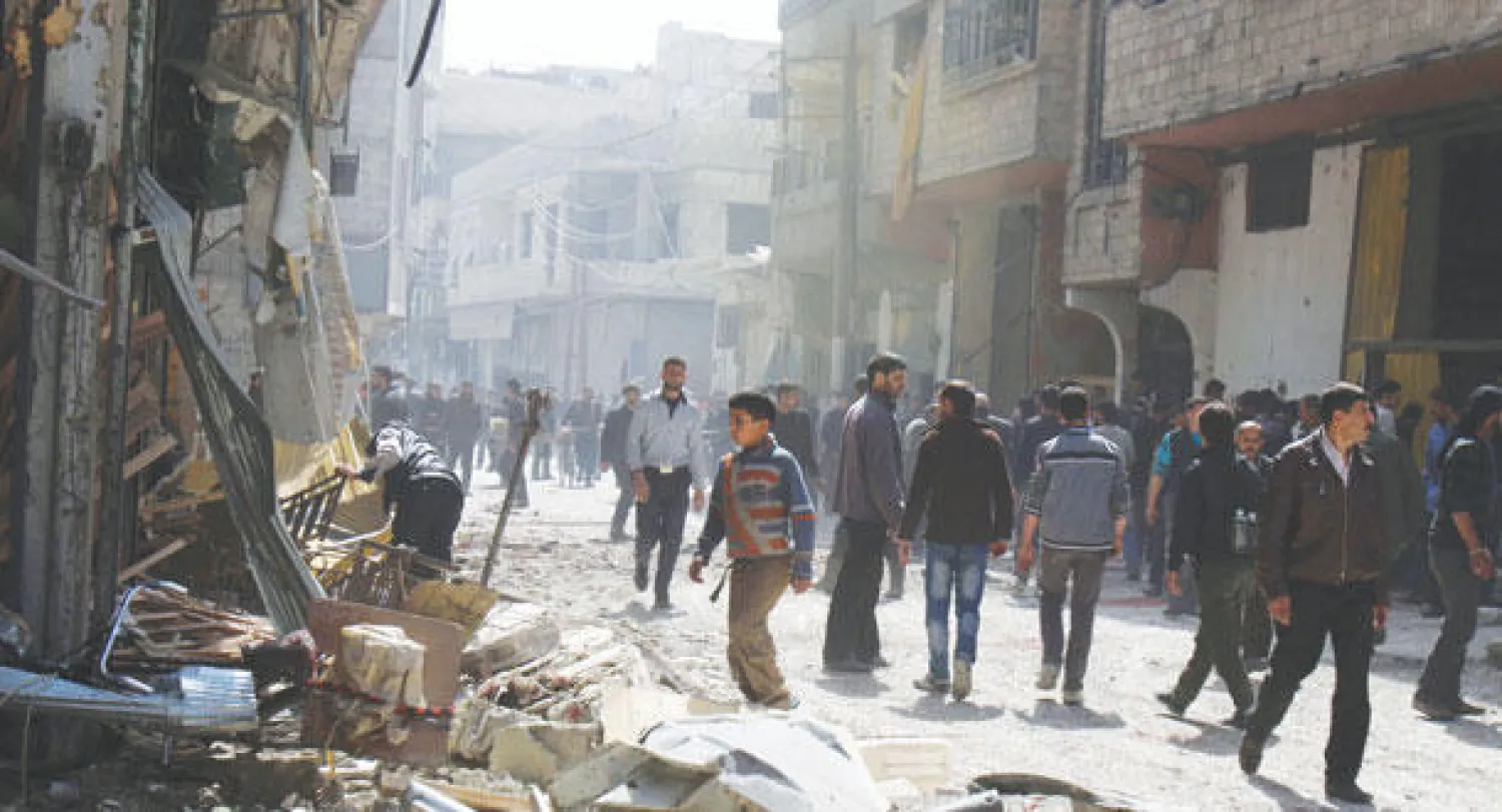 سكان بلدة عربين بريف دمشق الشرقي يتفحصون مبنى دمر على قاطنيه من قبل طيران النظام أمس (رويترز)