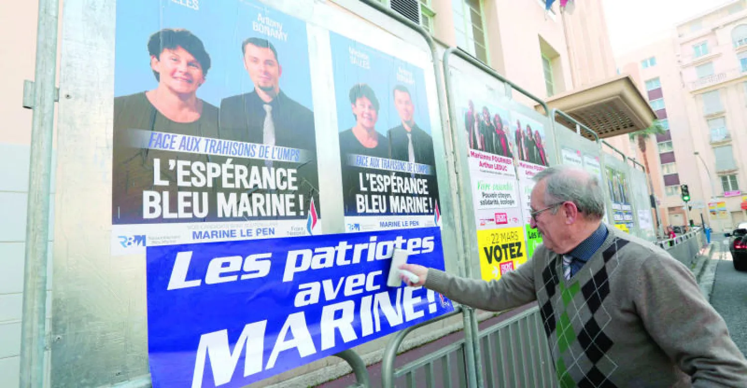 مناصر للجبهة الوطنية (اليمين المتطرف) يضع إعلانا انتخابيا مكتوبا عليه «الوطنيون مع مارين» في مدينة نيس عشية الانتخابات المحلية (رويترز)
