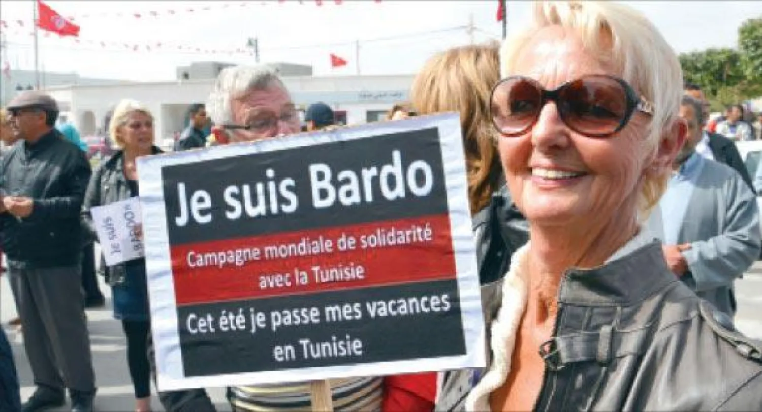 سياح أوروبيون شاركوا في مظاهرات ضد الإرهاب أمس وفي الصورة امرأة تحمل لافتة باللغة الفرنسية تقول: «أنا باردو وسأقضي الصيف المقبل في تونس» في جزيرة جربة التونسية أمس (أ.ف.ب)