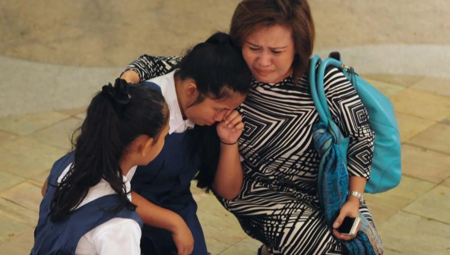 أم سنغافورية تواسي بنتيها بعد أن وضعن إكليلاً من الزهور أمام المستشفى العام السنغافوري حيث توفى لي كوان يو (أ.ف.ب)