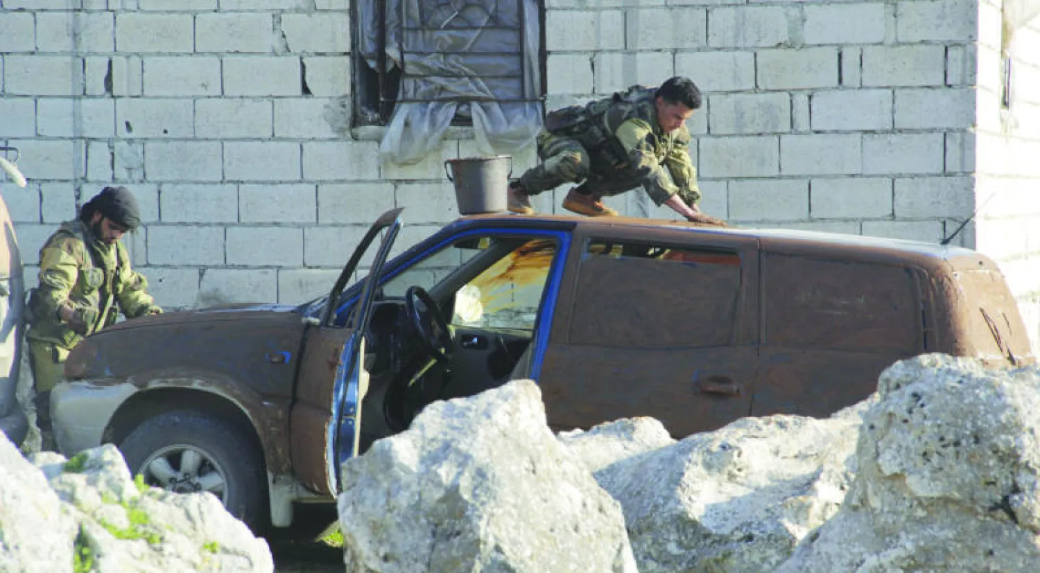 مقاتلون من لواء «أنصار الشام» يحاولون طلي سيارة عسكرية بالطين لإخفائها عن العيان قرب جسر الشغور بمحافظة إدلب (رويترز)