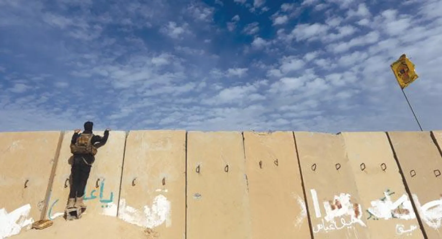 عنصر أمن عراقي يراقب من وراء جدار إسمنتي اشتباكات مع مسلحي «داعش» في تكريت أول من أمس (أ.ف.ب)