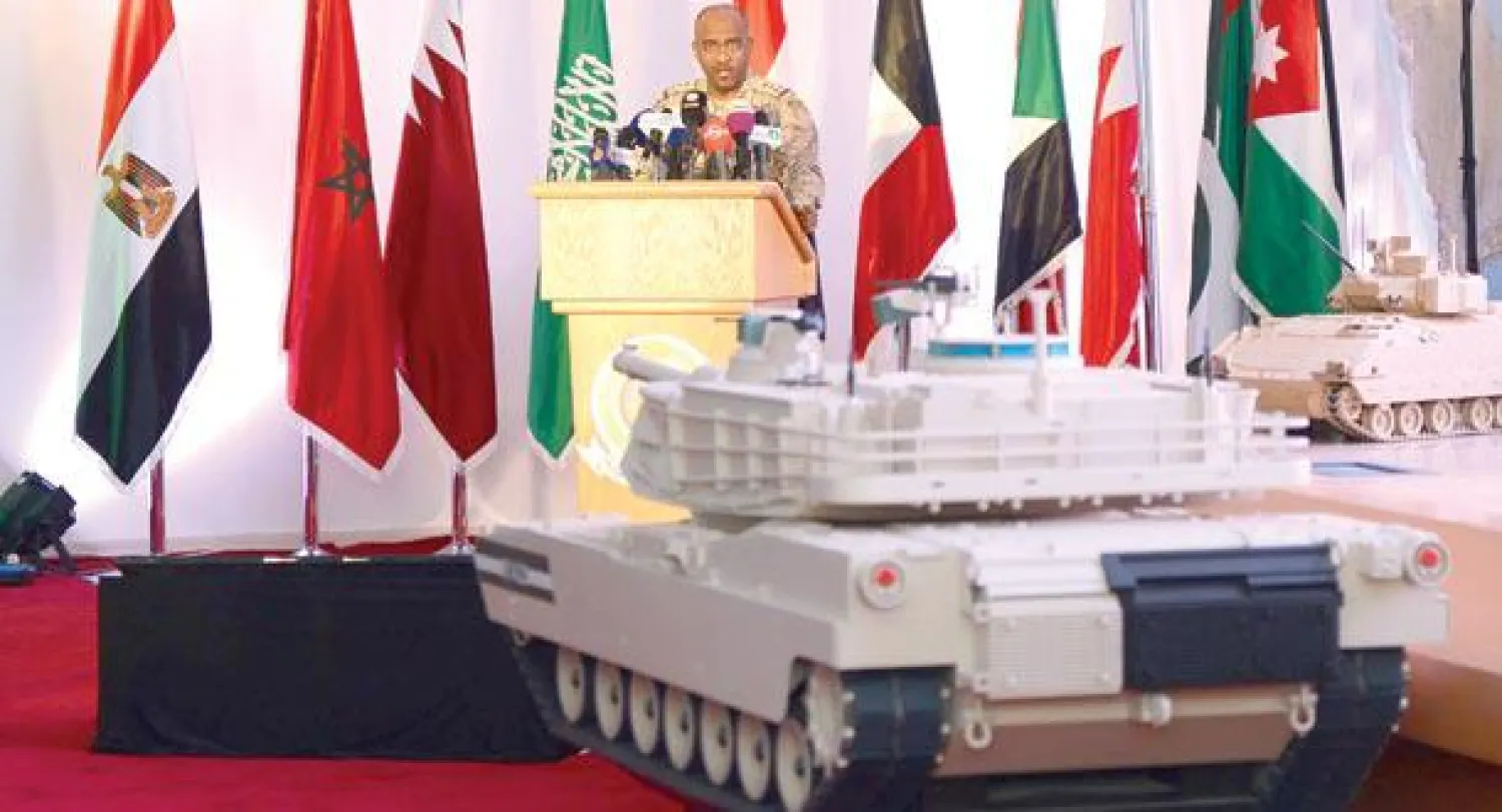 العميد أحمد عسيري خلال الإيجاز العسكري وبدت من خلفه أعلام الدول المشاركة في عملية {عاصفة الحزم} في يومها السادس (واس)