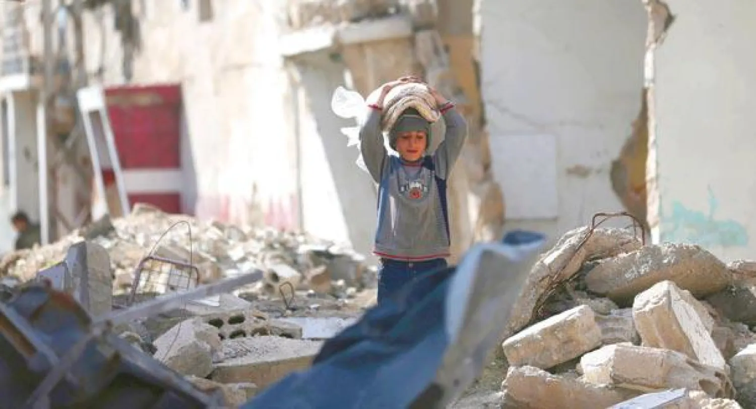 طفل من دوما بريف دمشق يحمل خبزا على رأسه ويسير عبر ركام الأبنية التي دمرها طيران النظام السوري (رويترز)