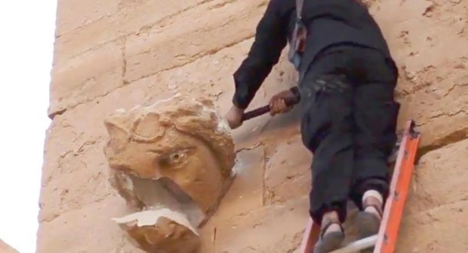 لقطة من فيديو بث على «يوتيوب» تظهر أحد عناصر «داعش» وهو يحاول إزالة قطعة منحوتة من جدار مبنى في موقع الحضر الأثري جنوب الموصل (أ.ب)