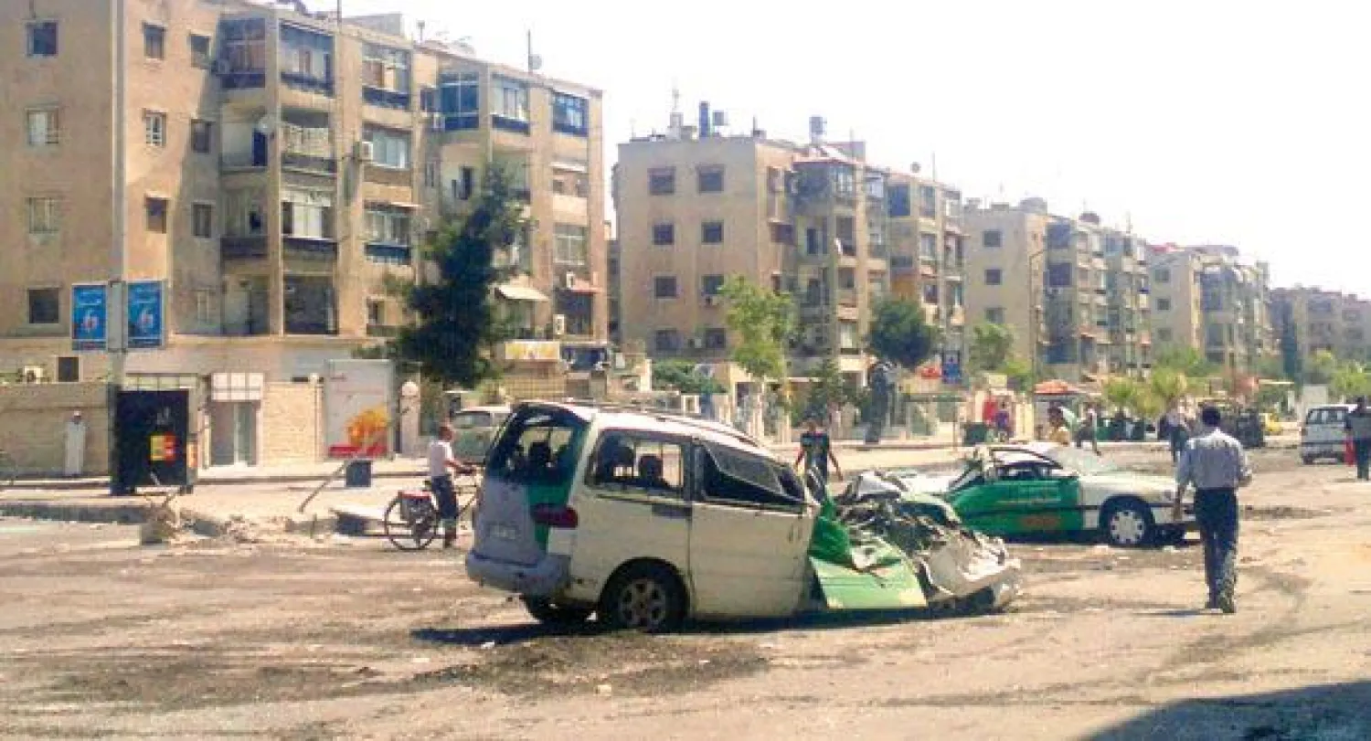 سوري يسير بالقرب من سيارتين محطمتين نتيجة الاشتباكات بين قوات النظام وعناصر {داعش} و{النصرة} في مخيم اليرموك جنوب دمشق أمس (أ.ب)