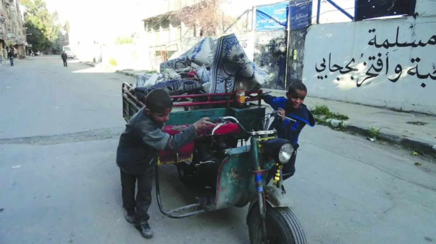 طفلان من مخيم اليرموك يجران عربة حملا عليها أغراضهما هربا من القتال العنيف (أ.ف.ب)