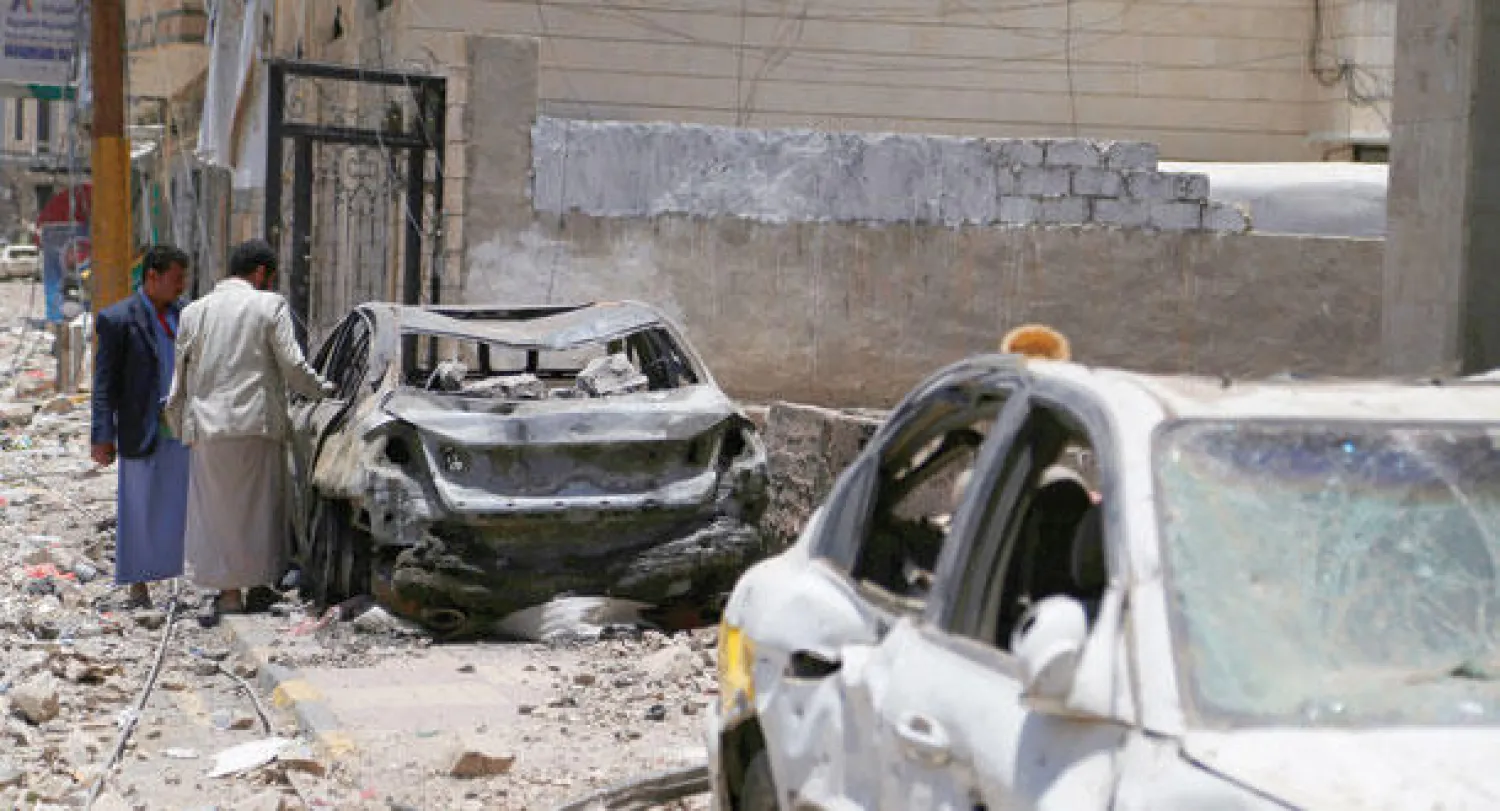 يمنيان يتفقدان سيارات تعرضت للتفجير بعد قصف قوات التحالف لمخازن تابعة للحوثيين (أ.ب)