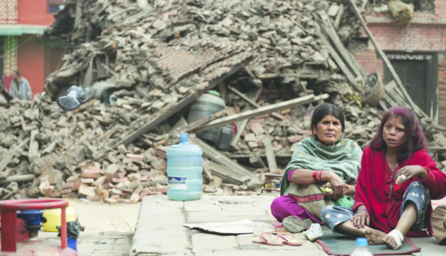 سيدتان نيباليتان تجلسان أمس أمام حطام منزليهما المدمرين إثر الزلزال القوي الذي ضرب منطقة بهاكتابور في كاتماندو (إ.ب.أ)