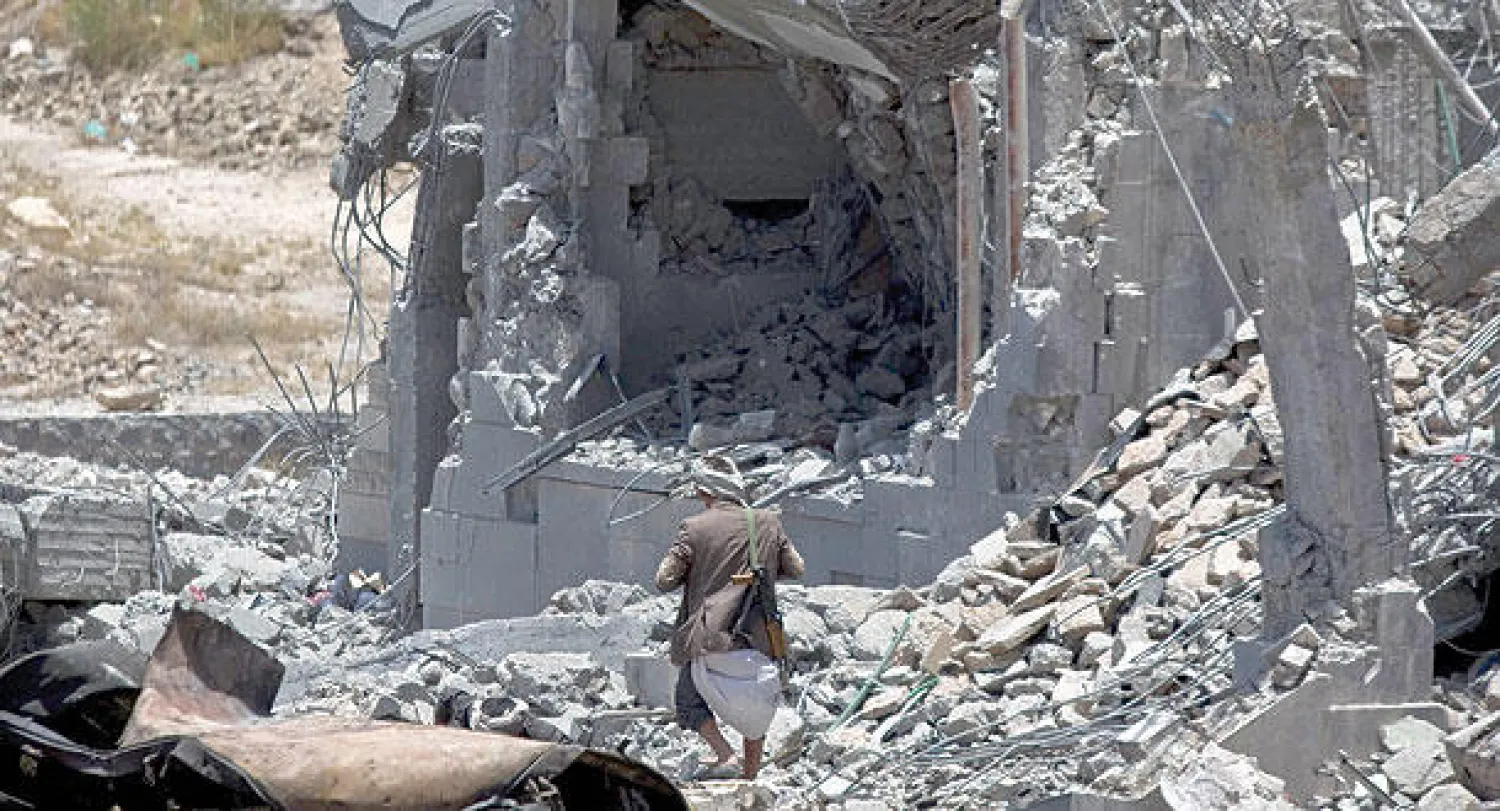 مقاتل حوثي يمشي على ركام أحد مقرات القيادة الحوثية استهدفها طيران التحالف في صنعاء أمس (أ.ب)