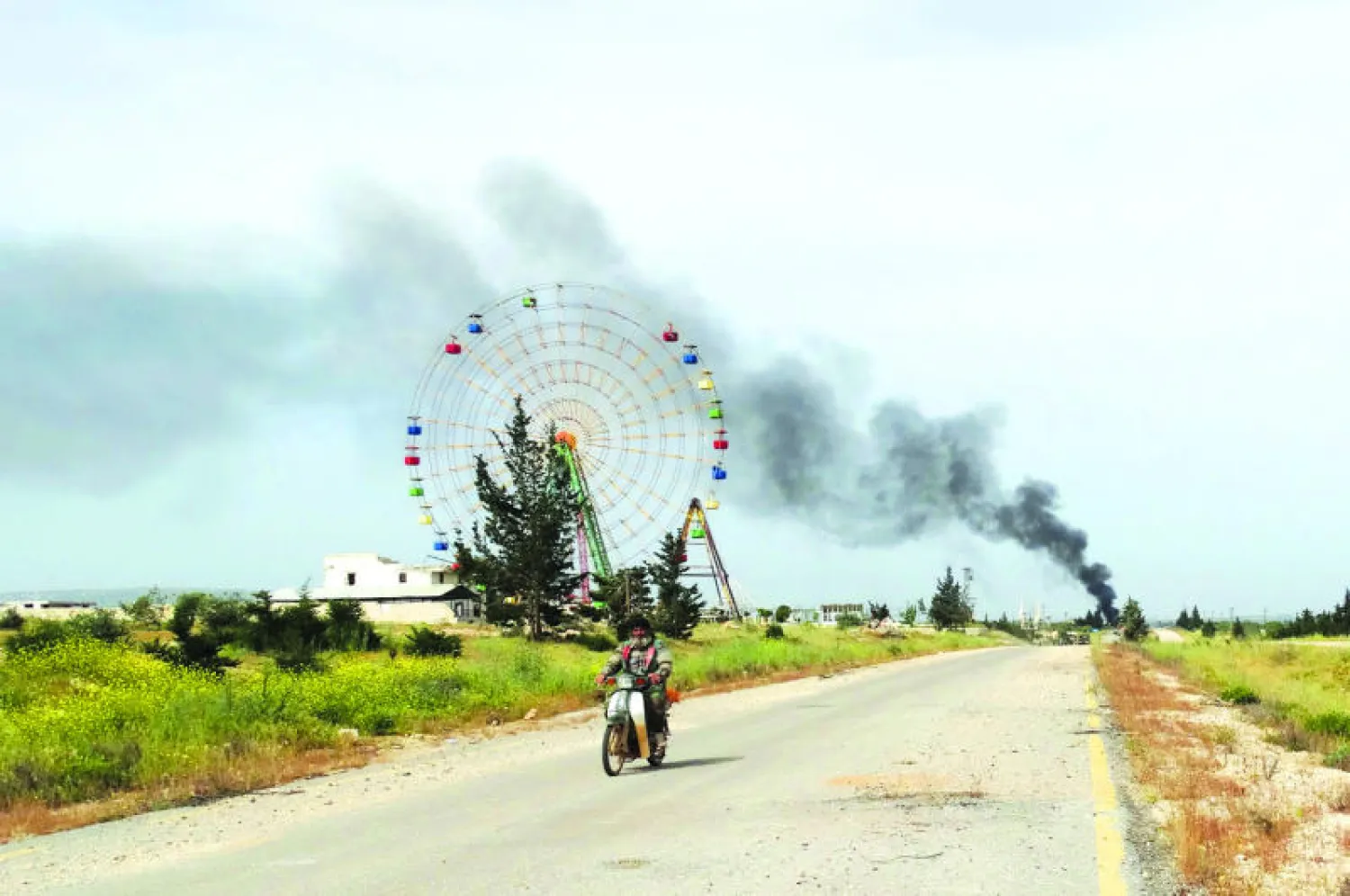 مقاتل من المعارضة ويبدو خلفه الدخان المتصاعد من «معسكر القرميد» بريف إدلب بعد السيطرة عليه ودحر قوات النظام منه أول من أمس (رويترز)