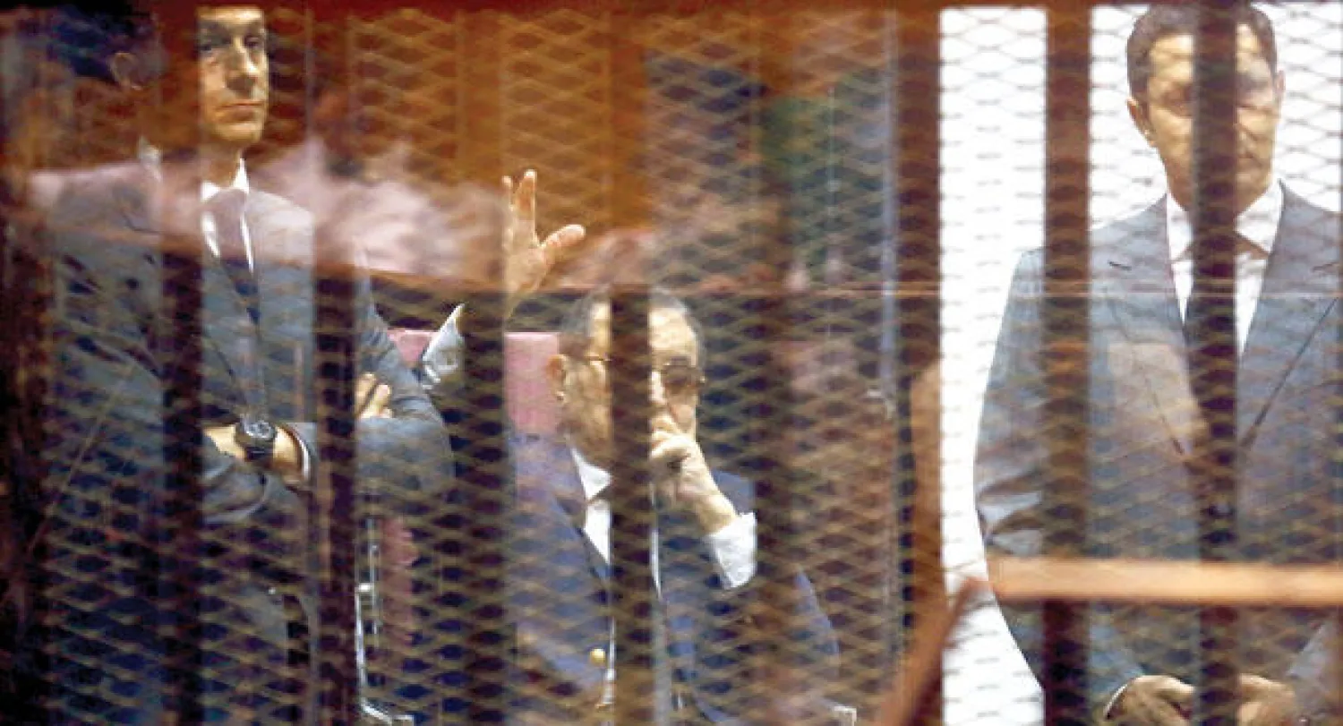 الرئيس السابق حسني مبارك يحيي مؤيديه بين ولديه علاء وجمال خلف القضبان في المحكمة الجنائية أمس (رويترز)