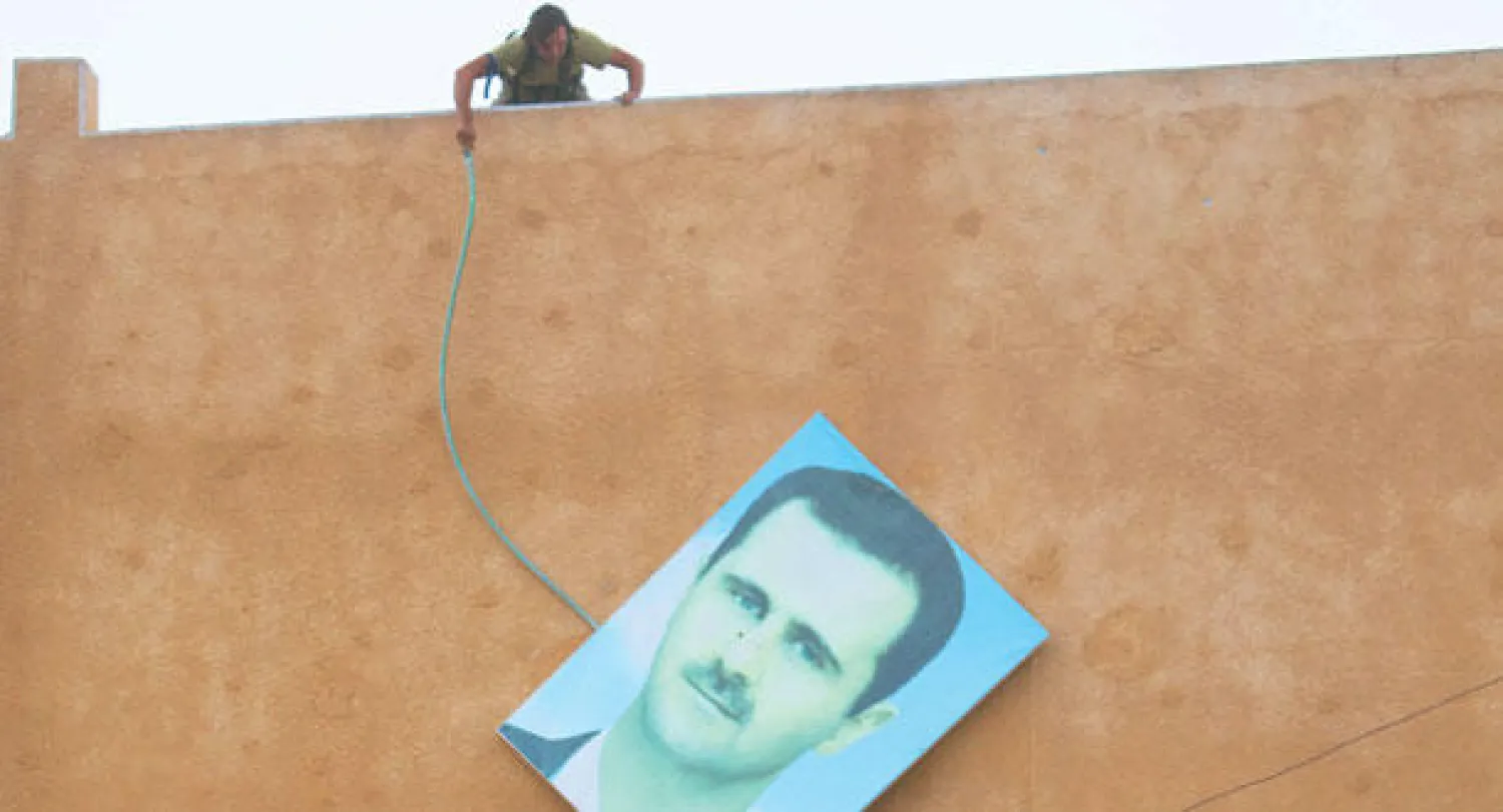 عنصر من جبهة النصرة ينزل صورة لبشار الأسد في أريحا بعد سيطرة الجبهة عليها أمس (رويترز)