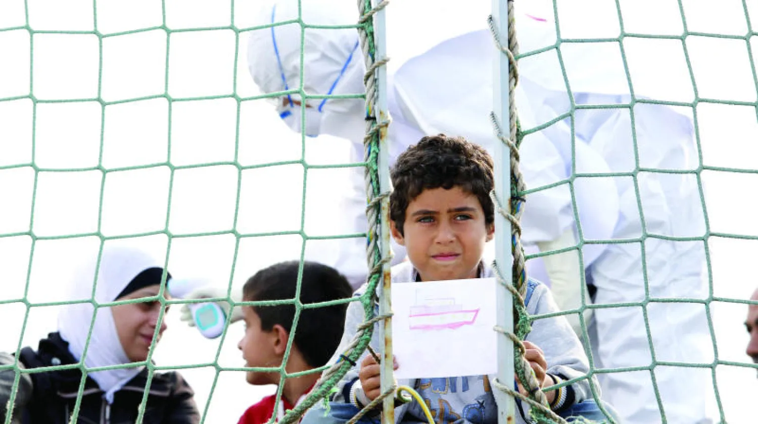 طفل سوري يعرض رسما بينما ينتظر النزول إلى رصيف ميناء أوغوستا الإيطالي ضمن مجموعة من مهاجري البحر أنقذتهم ناقلة بحرية بلجيكية (رويترز)