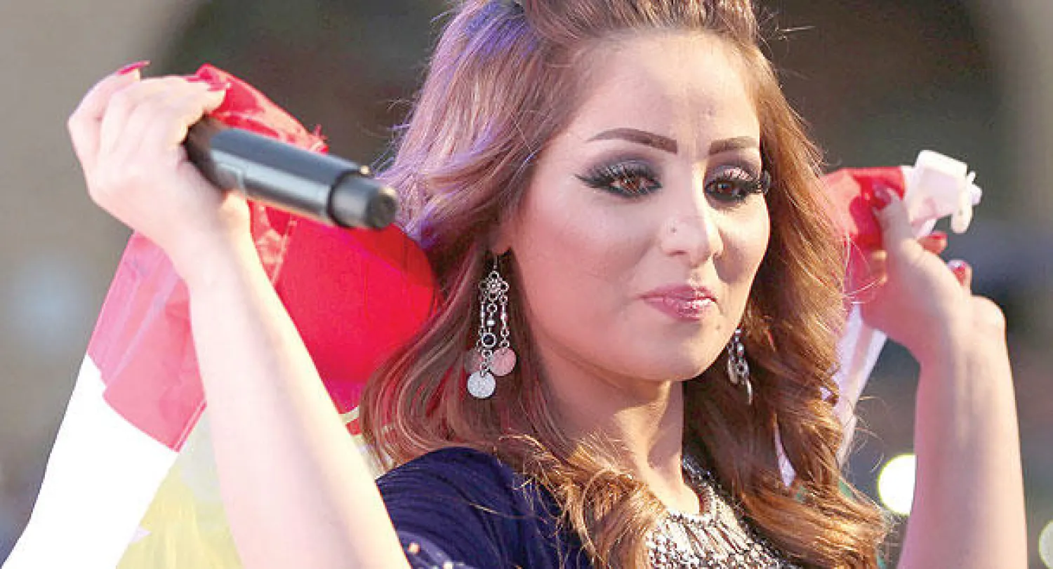 المغنية الكردية برواز حسين تضع علم إقليم كردستان على كتفها وتغني ضمن احتفالية «متحدون مع التراث» في أربيل أمس (أ.ف.ب)