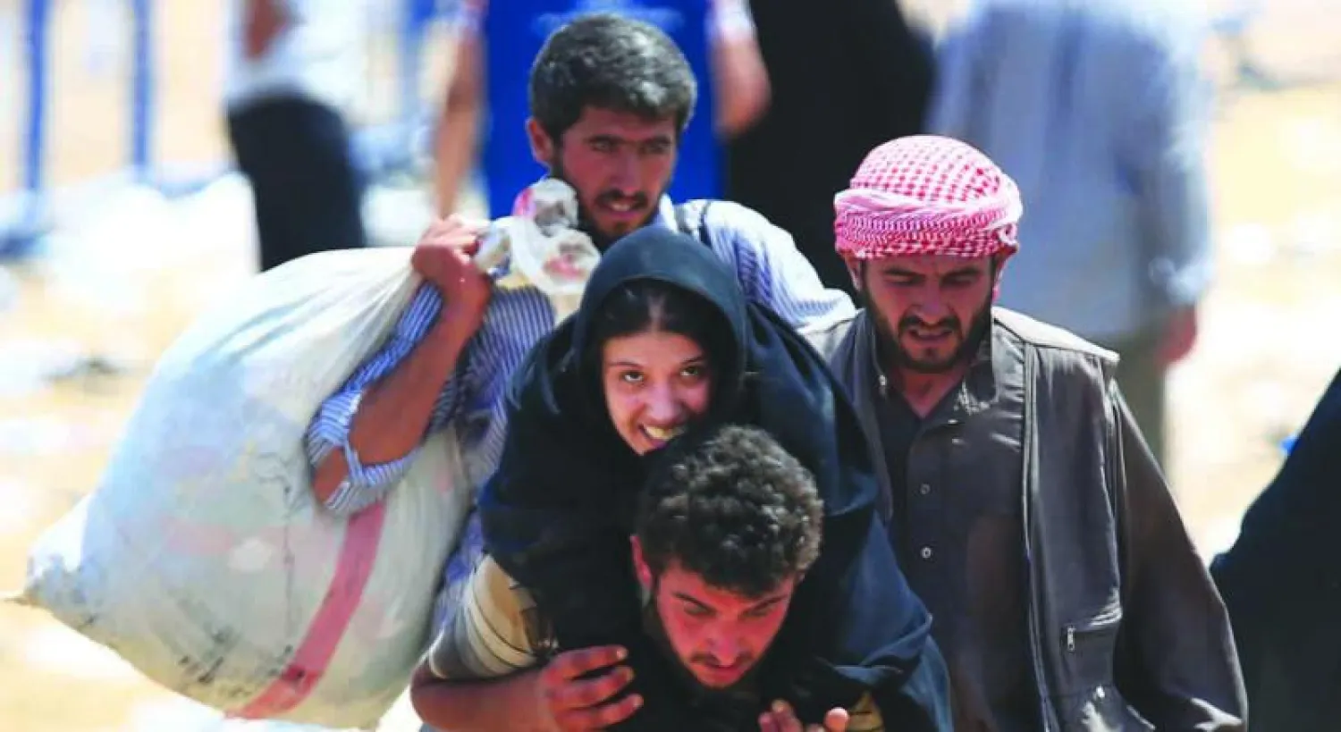 سوري يحمل امرأة على ظهره باتجاه الأراضي التركية بعد نزوح سكان تل أبيض من الحرب ضد «داعش» (أ.ب)