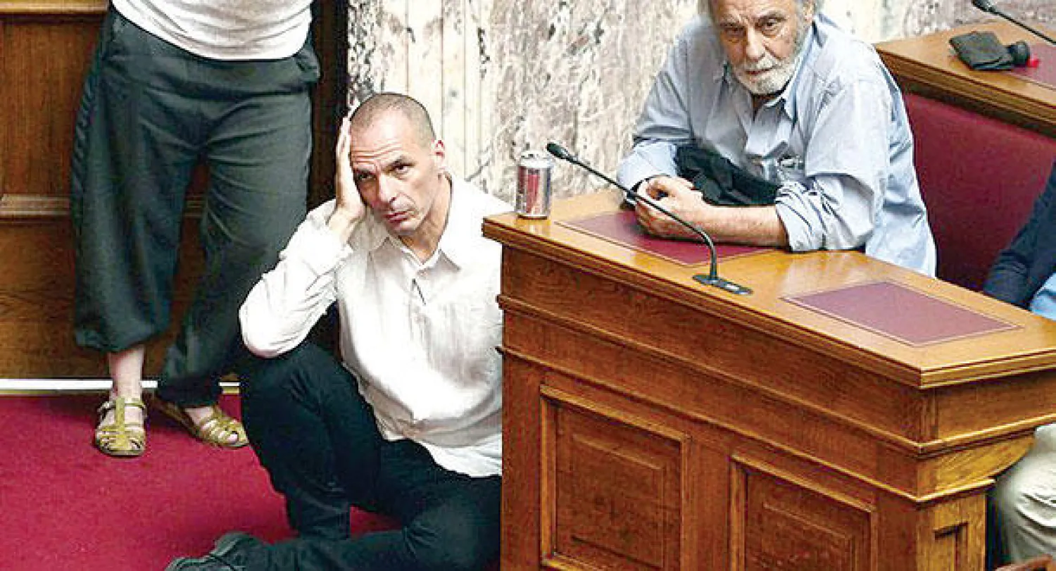 وزير المالية اليوناني يانيس فاروفيكيس يستمع جالسًا لخطاب رئيس الوزراء الكسيس تسيبيراس في البرلمان أول من أمس (أ.ف.ب)