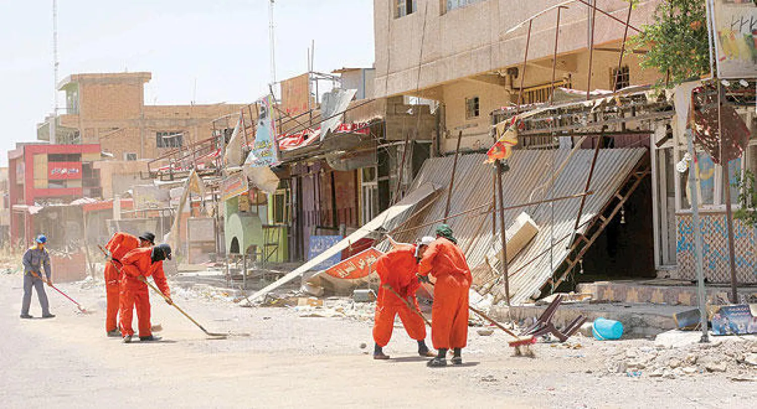 عمال البلدية يكنسون شارعا في تكريت مع عودة النازحين إليها (أ.ب)