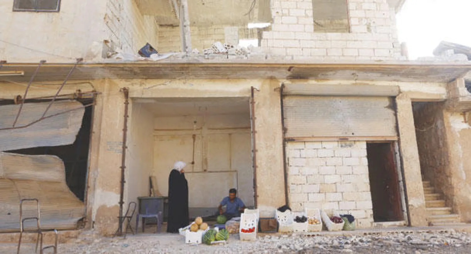 تاجر في بلدة قميناس بمحافظة إدلب السورية أمام بضاعته المعروضة بانتظار متسوقي شهر رمضان في خرائب شارع شهد آثار الحرب (رويترز)