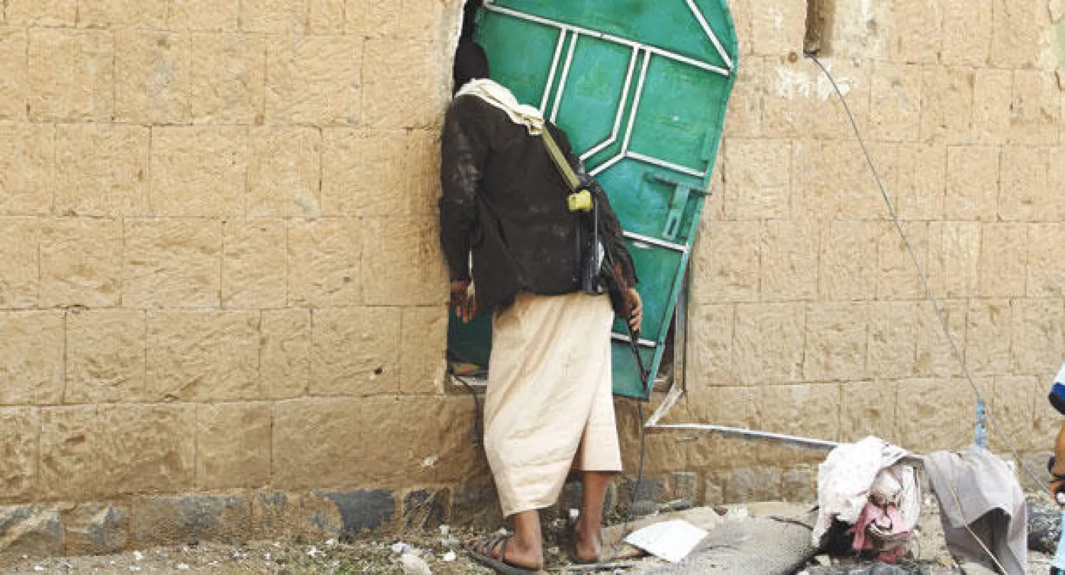 مسلح من المتمردين الحوثيين يتفقد منزلا بعد أن قصفته قوات التحالف أمس (إ.ب.أ)