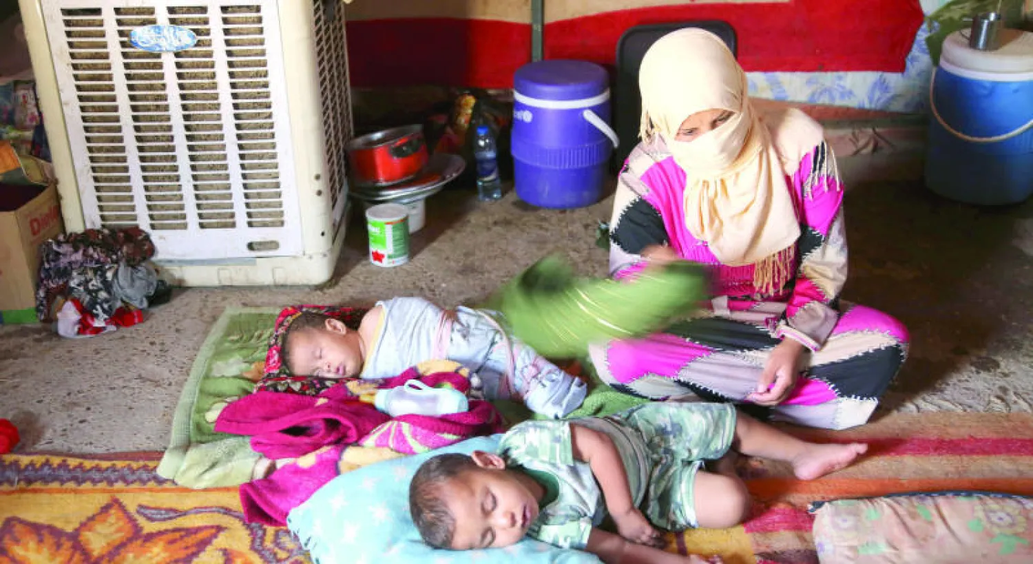 نازحة عراقية تخفف بمهفة وطأة الحر عن طفليها في مخيم للنازحين بالدورة جنوب بغداد أمس (أ.ب)