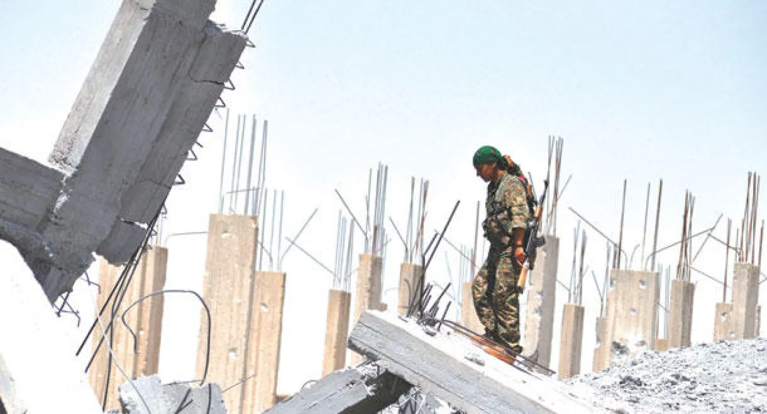 مقاتلة كردية ضمن وحدة الدفاع الشعبي تنظر إلى آثار الدمار في مدينة عين عيسي بالقرب من الرقة والتي خلفتها المواجهات بين الأكراد وداعش (أ.ف.ب)