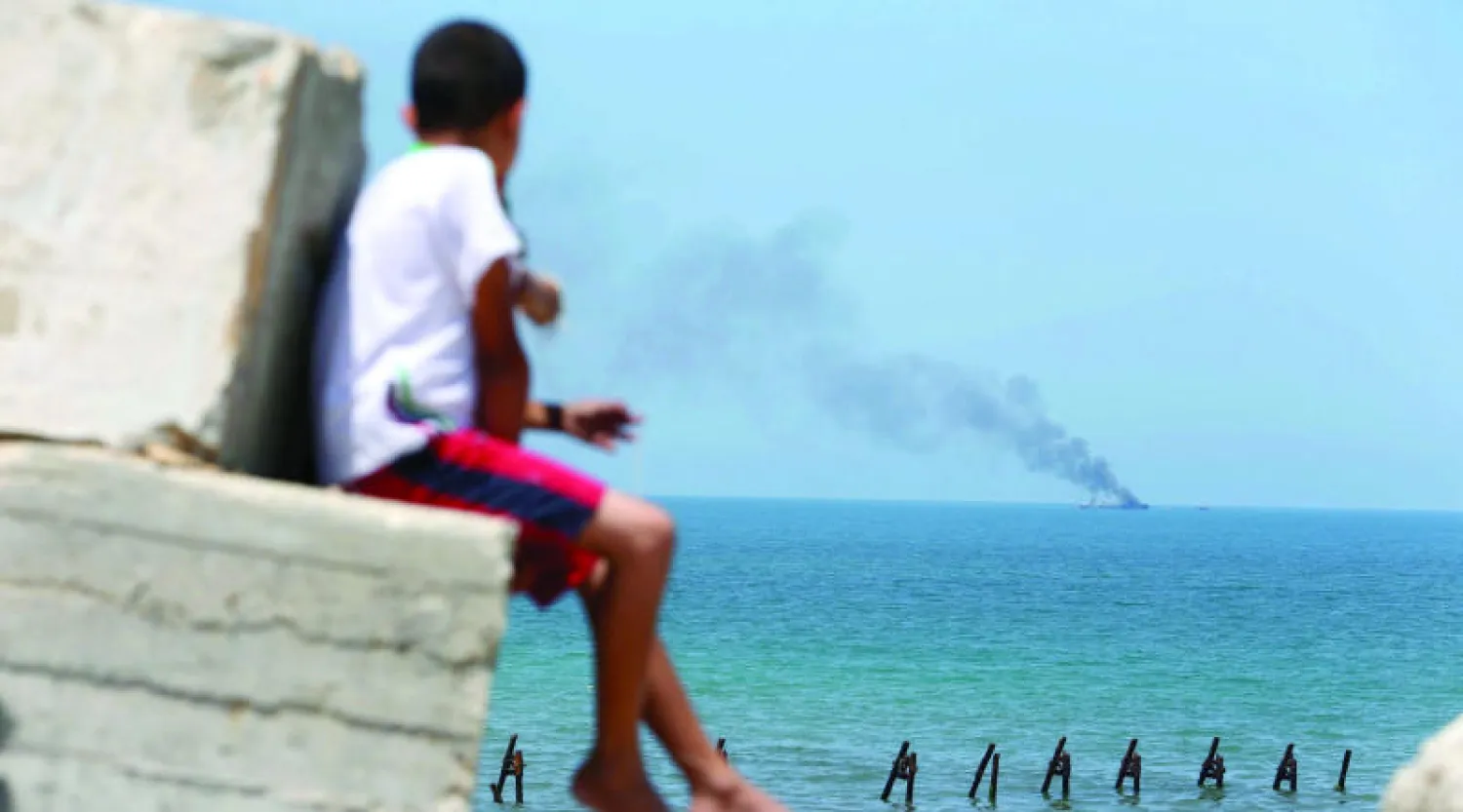 أطفال فلسطينيون يشاهدون دخان زورق عسكري تعرض للحرق أمام ساحل رفح.. وأعلن تنظيم «ولاية سيناء» التابع لتنظيم داعش في مصر مسؤوليته عن تلك العملية (رويترز)