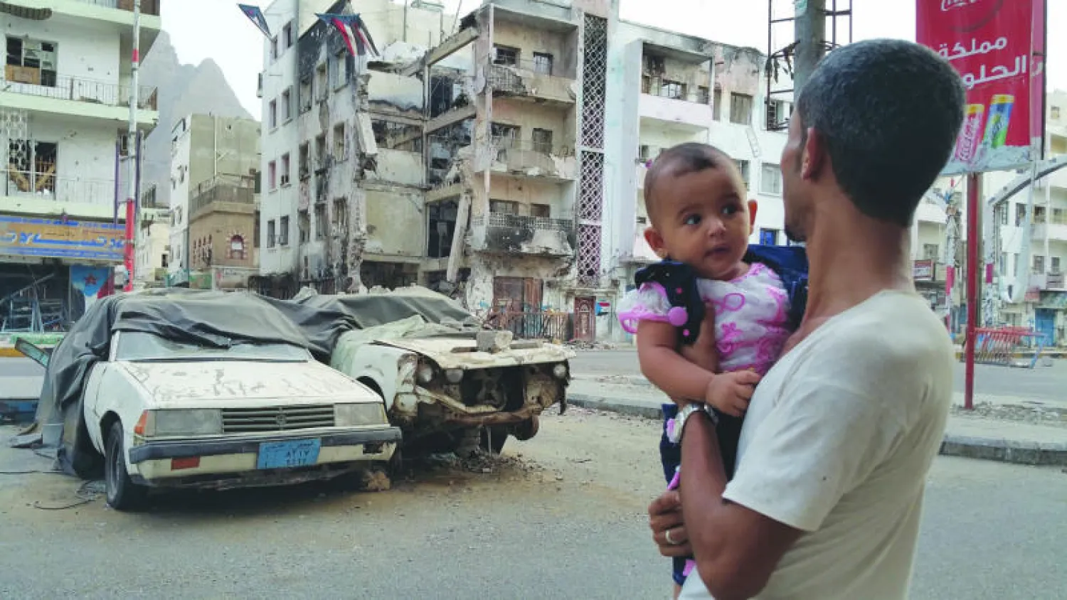يمني يحمل ابنته أمام مبنى دمر في حي التواهي جراء  القتال الدائر بين المقاتلين الحوثيين  والمقاومة الشعبية بمدينة عدن الجنوبية (أ.ف.ب)