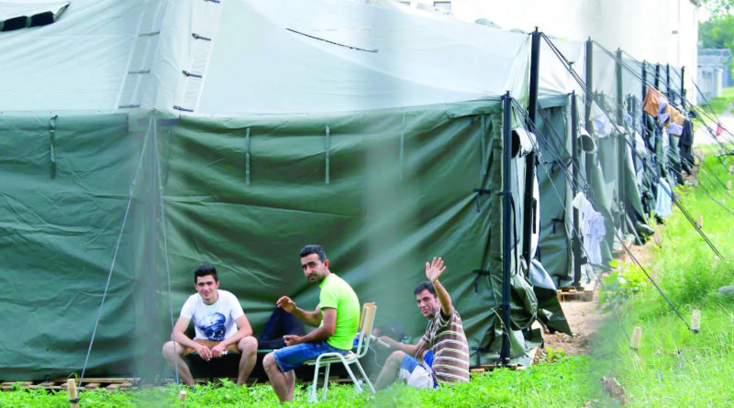 لاجئون سوريون يجلسون خارج خيمة في مركز أعد لهم في ألمانيا (رويترز)