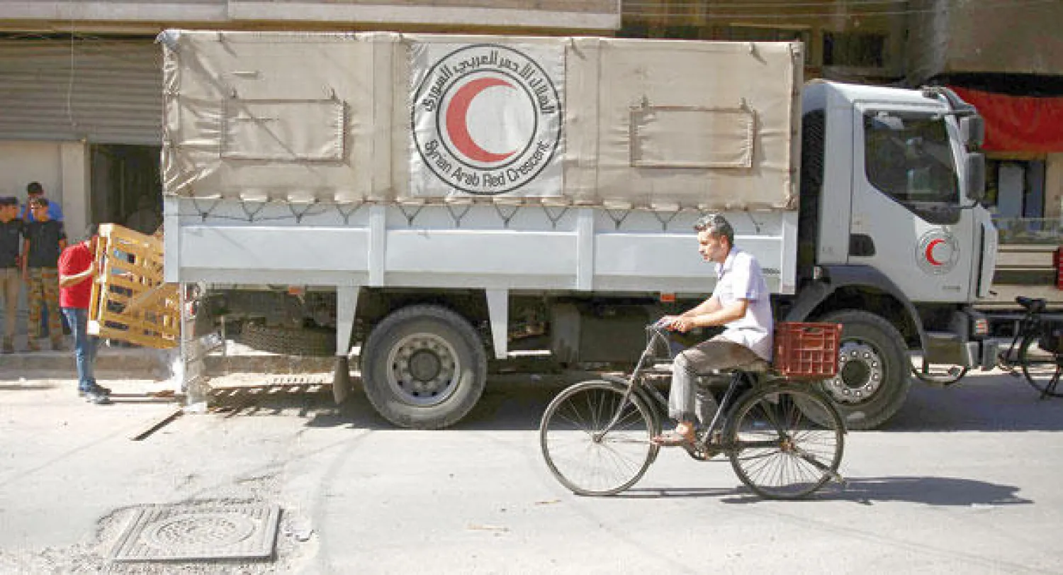 رجل من دوما بريف دمشق يمر بدراجته بجانب شاحنة تابعة للهلال الأحمر السوري التي توزع الأدوية واللقاحات في المدينة المحاصرة من قبل النظام. (أ.ف.ب)