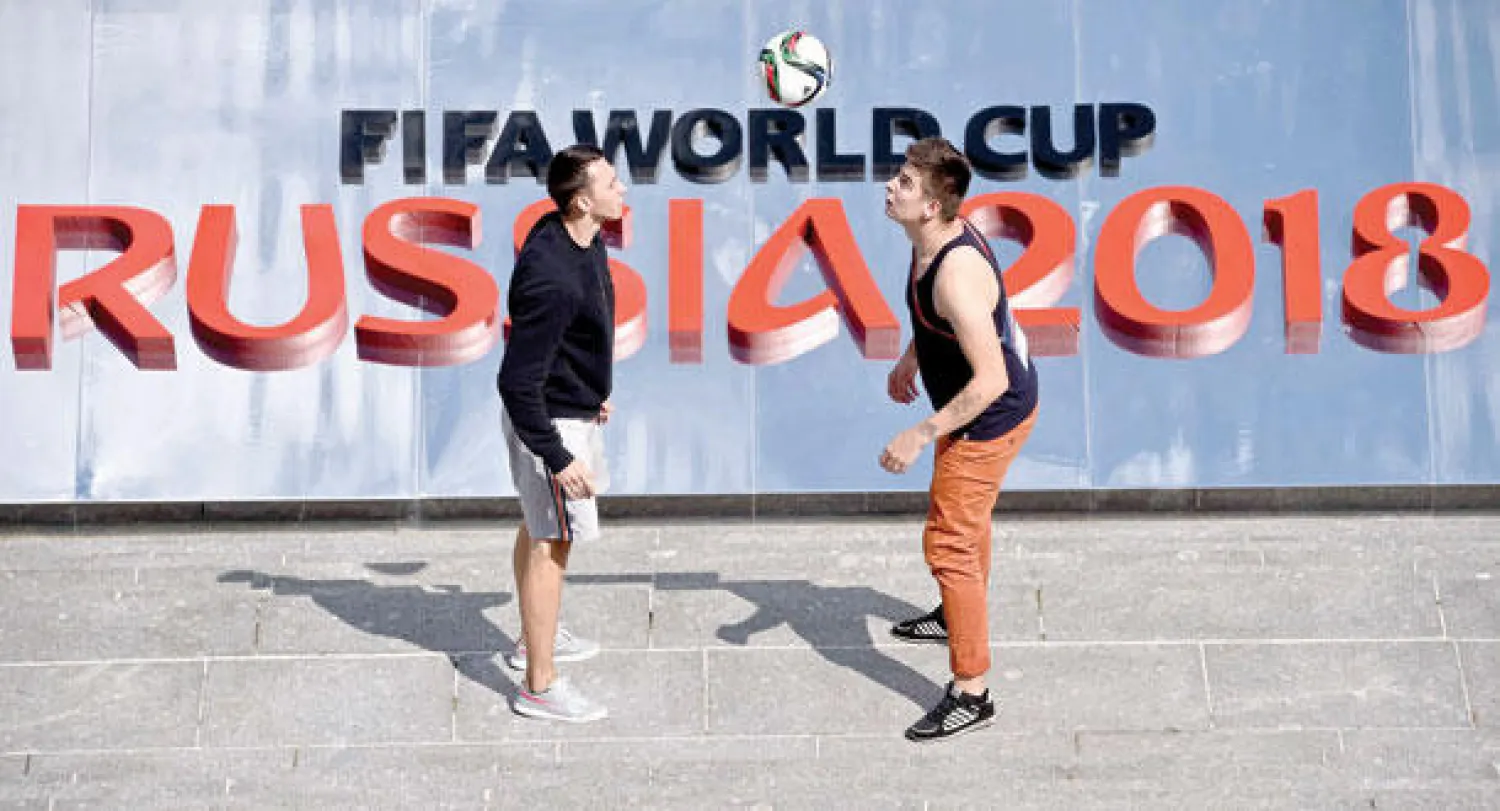 شابان يلعبان بكرة أمام لافتة تروج لقرعة كأس العالم 2018 التي تجرى اليوم في سان بطرسبرغ (أ.ف.ب)