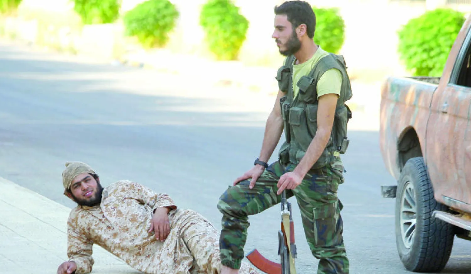 مقاتلان من جيش الفتح يستريحان مع أسلحتهما قرب محطة زيزون الحرارية في سهل الغاب بريف حماه (رويترز)