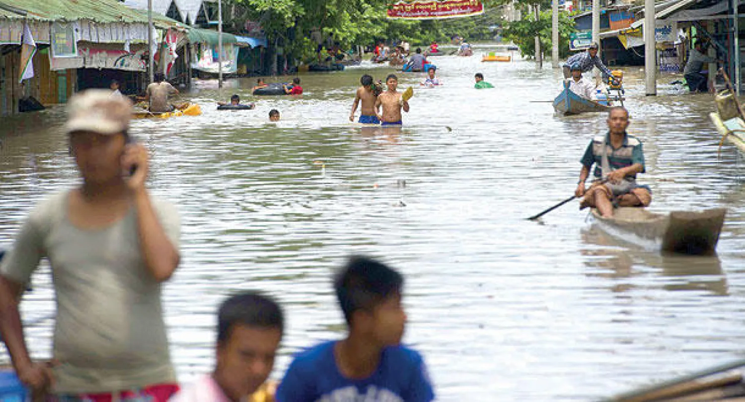 مواطنون يركبون قوارب على شارع أغرقته مياه الفيضان في منطقة كالاي بميانمار أمس (أ.ف.ب)