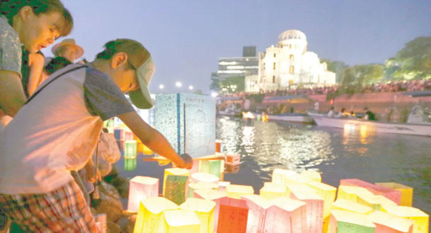 صبي يحرك فوانيس ورقية على نهر موتوياسو لضحايا الهجوم الذري أمام قبة القنبلة الذرية في حديقة السلام في هيروشيما أمس (إ.ب.أ)