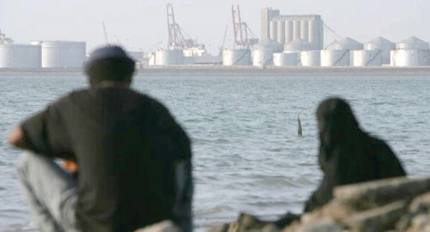 يمنيان يجلسان بالقرب من مستودع للنفط بميناء محافظة الحديدة اليمنية المطلة على بحر العرب وخليج عدن والبحر الأحمر (غيتي)