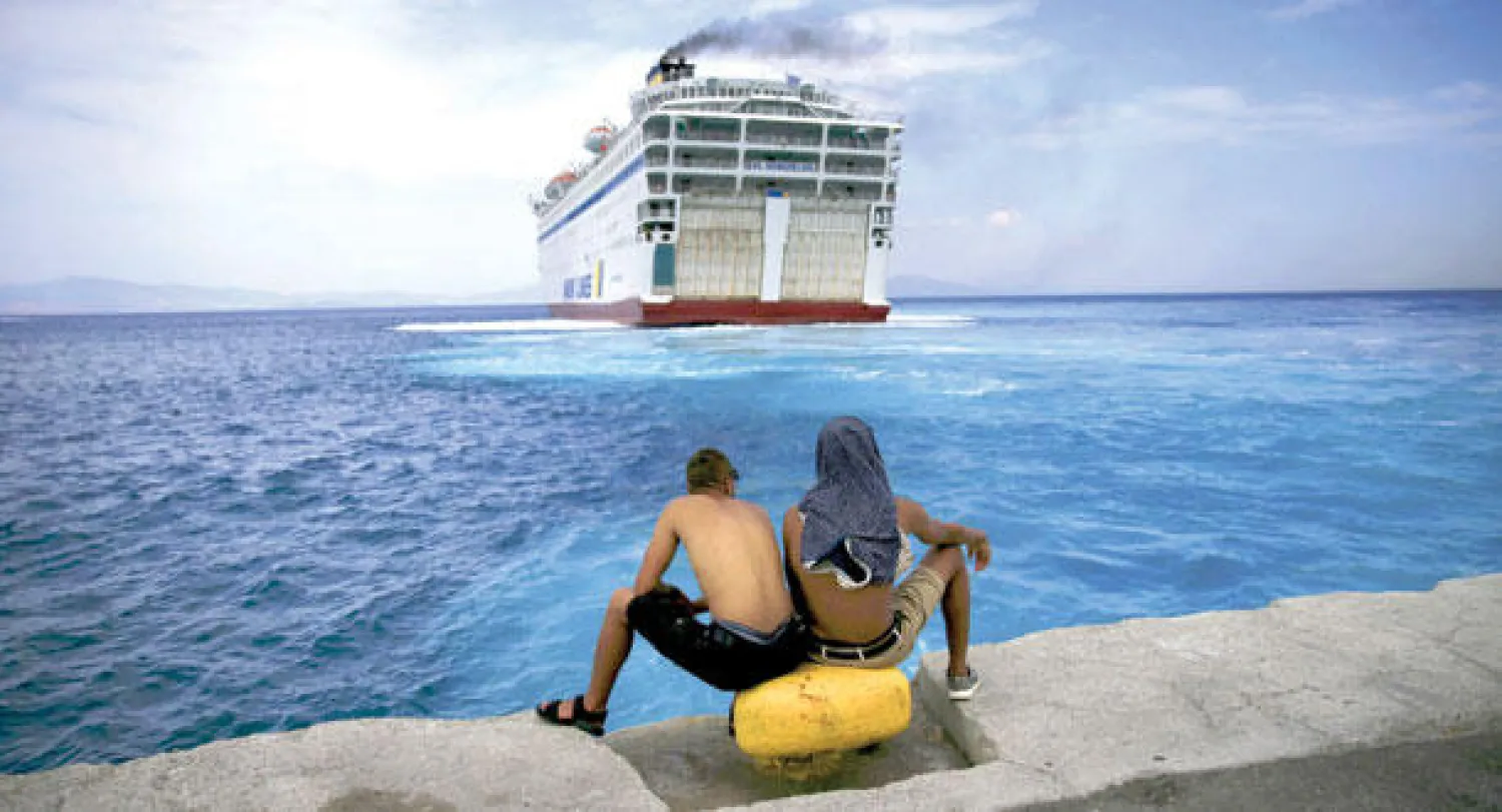 لاجئان سوريان عالقان على ضفاف جزيرة كوس اليونانية بعد وصولهما من تركيا في وقت ذكرت فيه المنظمة الدولية للهجرة أمس أن نحو 239 ألف شخص فروا من الصراعات والفقر عبروا البحر المتوسط إلى أوروبا حتى الآن هذا العام (رويترز)