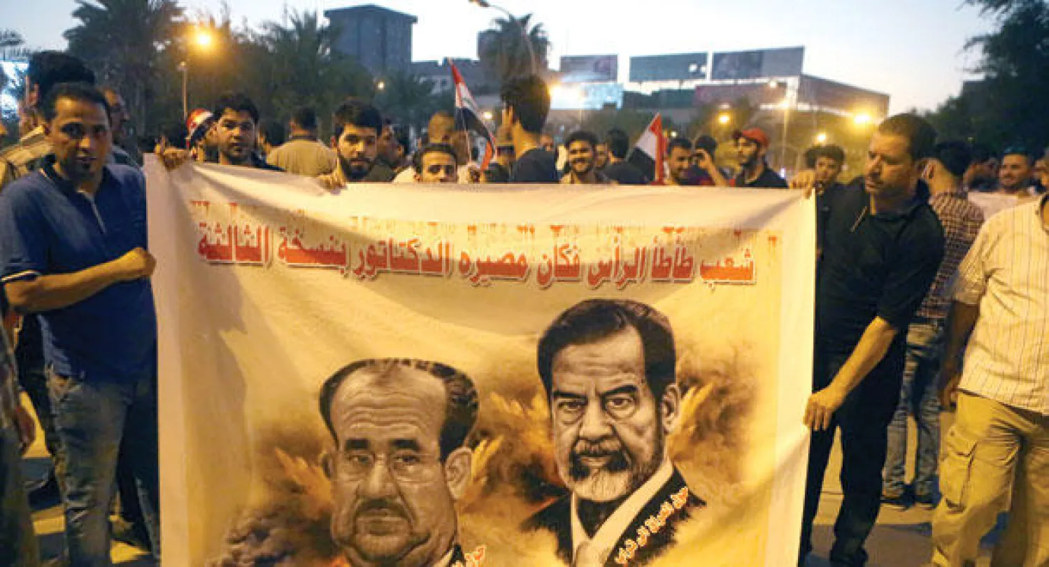 متظاهرون يحملون لافتة عليها صورتا الرئيس العراقي الأسبق صدام حسين ورئيس الوزراء السابق نوري المالكي في ساحة التحرير ببغداد مساء أول من أمس (أ.ب)