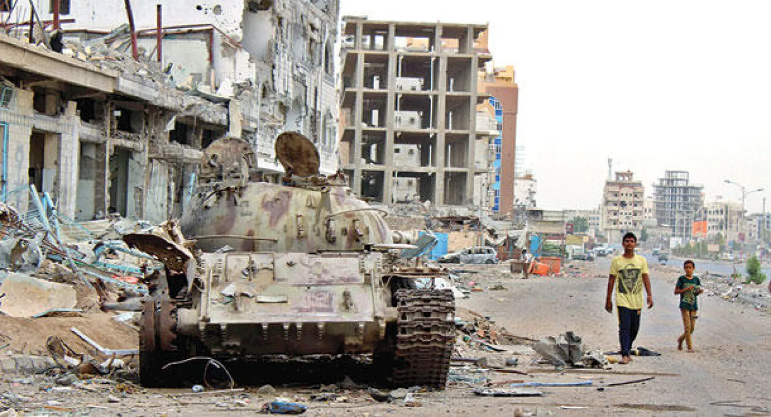 يمنيون يتجولون أمس إلى جانب دبابة ومبان دمرتها الاشتباكات التي شهدتها عدن بين الميليشيات الحوثية والمقاومة (إ.ب.أ)