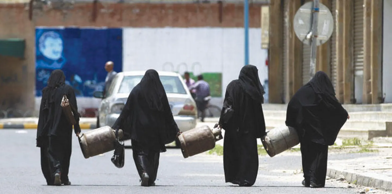 يمنيات يسرن نحو محطة وقود من أجل شراء بديل لاسطوانات الغاز الفارغة التي يحملنها (أ.ف.ب)